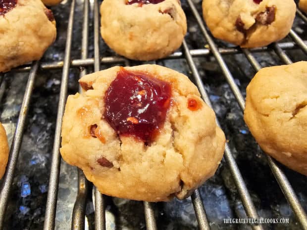 A close up of one of the raspberry thumbprint cookies on a wire rack.