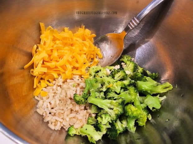 Cooked rice, broccoli, grated cheese and spices for stuffing, in a metal bowl.