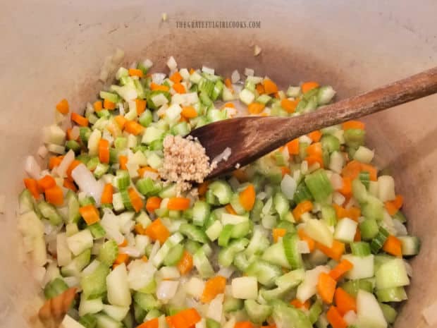 Minced garlic is added to the cooked veggies in the soup pot.