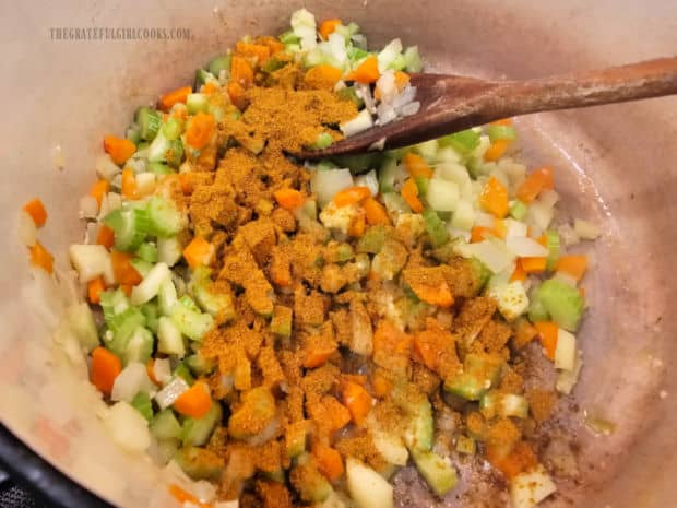 Curry powder is stirred into the sautéed vegetables in the soup pot.