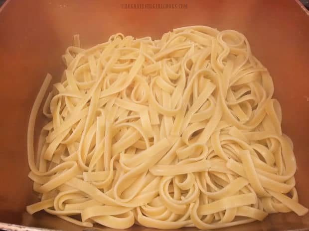 Cooked fettucine pasta is drained after cooking and put back into hot pan.
