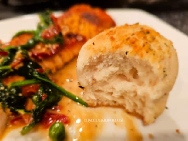 One of the garlic butter herb rolls on a white plate, with salmon in background.