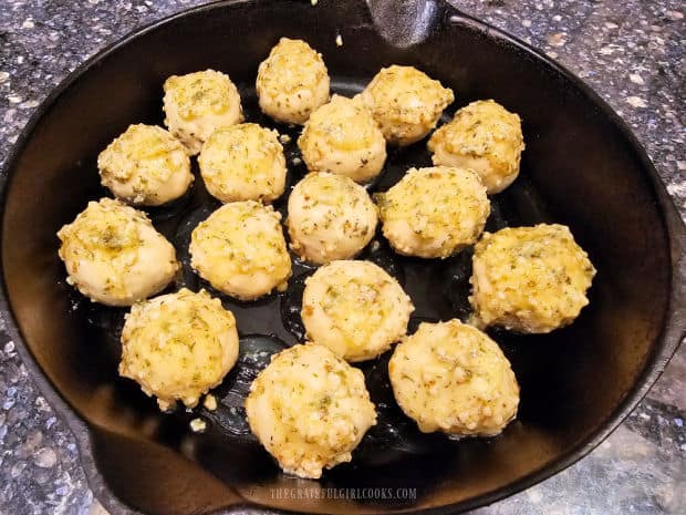 Sixteen butter and herb covered rolls are placed in a cast iron skillet.