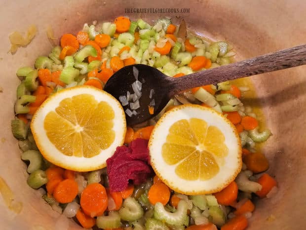 Orange slices, oregano, tomato paste and bay leaf are added to soup pot.