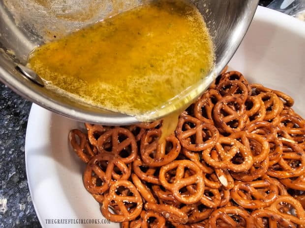 Seasoning sauce is poured over mini twist pretzels in a large bowl.