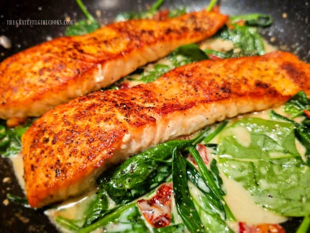Cooked salmon fillets are put back into skillet on top of the spinach sauce.