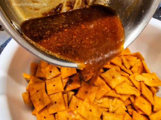 Seasoning mix is poured over the cheese crackers in a large white bowl.