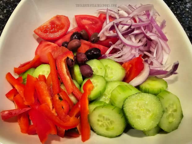 Cucumbers, red peppers, tomatoes, red onions and kalamata olives in salad bowl.