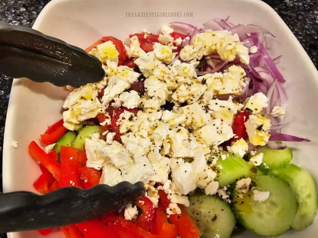 All the ingredients for the Greek salad are tossed together, using tongs.