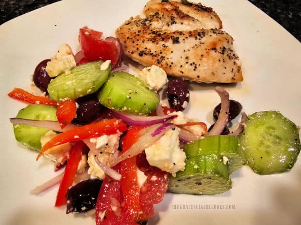 Traditional Greek Salad, served with chicken on the side, on a white plate.