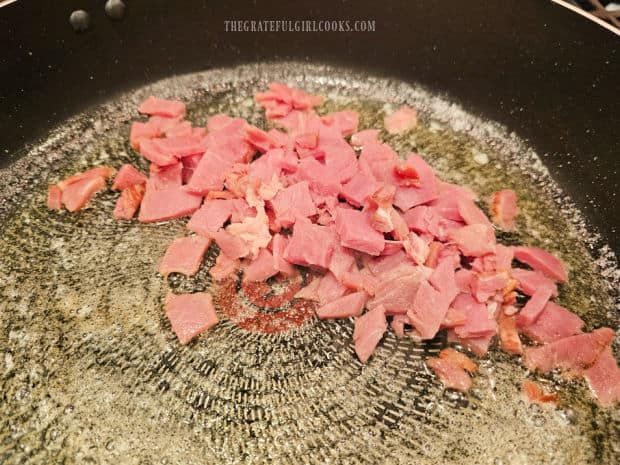 Cooked ham pieces are cooked in melted butter in a large skillet.