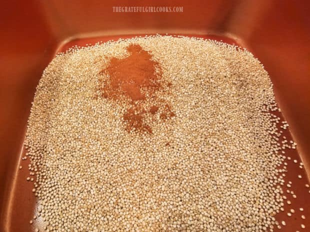 Uncooked quinoa and ground cinnamon are warmed in a saucepan.