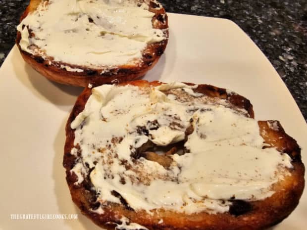 Cream cheese was spread on two toasted bagel halves, and are ready to eat.