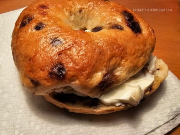 A chocolate chip bagel, filled with cream cheese, ready to be eaten.