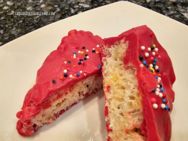 One of the chocolate covered krispie treats is shown cut in half, on white plate.