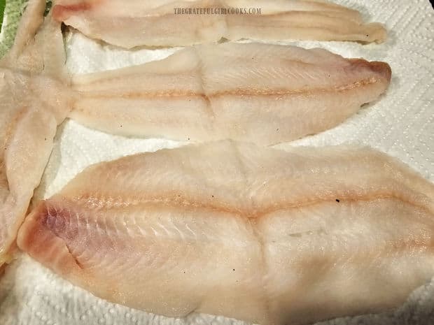 Four Dover sole fillets are patted dry using paper towels.