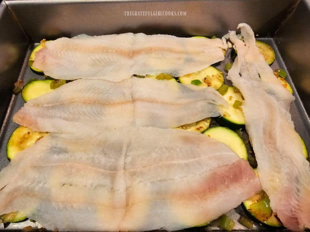 Dover sole fillets are placed on top of the zucchini slices in pan.