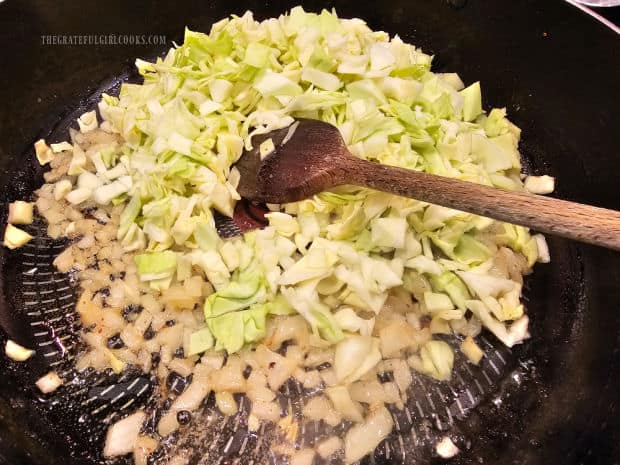 Chopped cabbage is added to the cooked onions and butter in skillet.
