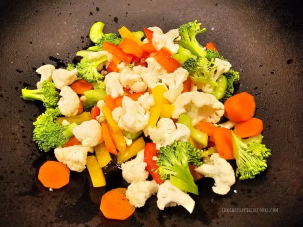 A variety of chopped vegetables are stir-fried in hot oil in a pan.