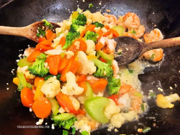 The cooked vegetables are added back into the stir-fried shrimp.