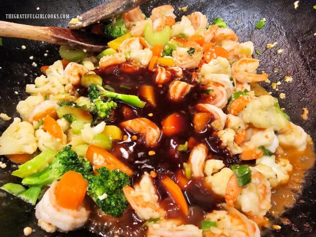 Szechuan sauce is added to the vegetables and shrimp in pan.
