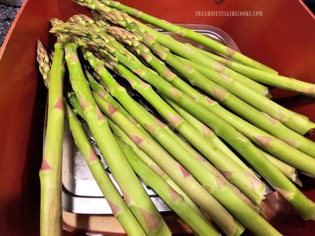 Fresh asparagus is steamed on a steamer basket over water in saucepan.