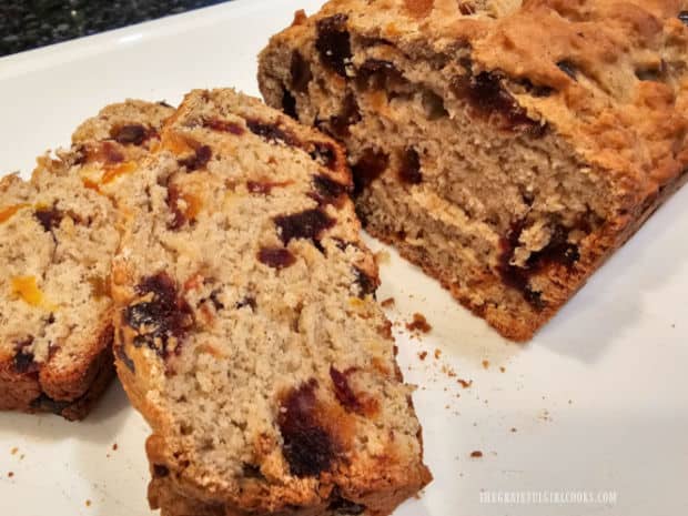 Two slices of banana apricot date bread, with remaining loaf in background.