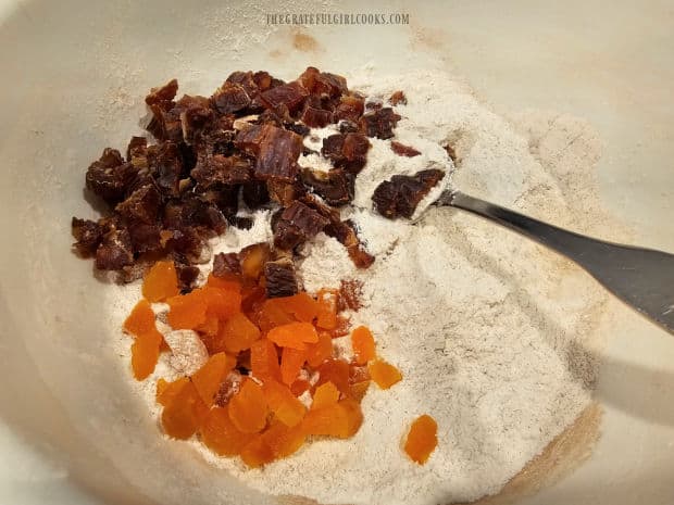 Dried, chopped dates and apricots are added to flour mixture in bowl.