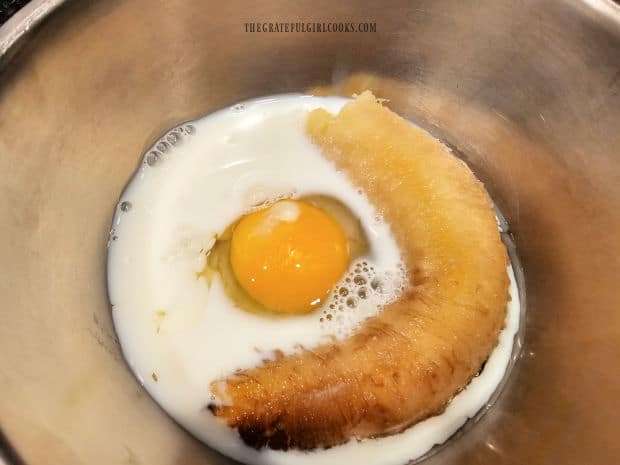 A ripe banana, an egg and milk in a bowl, ready to be mashed and beaten.