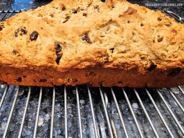 A side view of a loaf of banana apricot date bread, cooling on a wire rack.