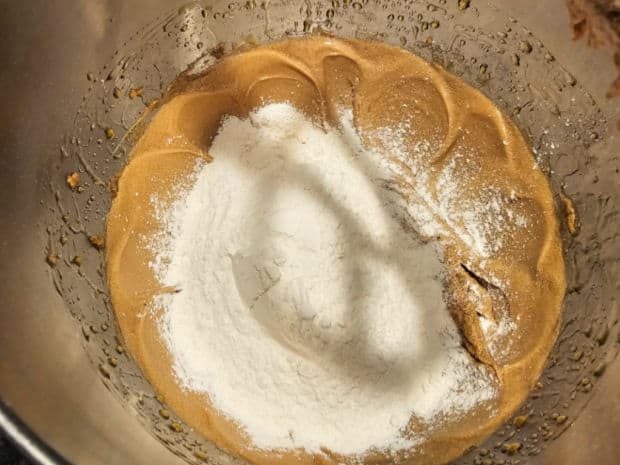 Dry ingredients are added to the cookie batter in a bowl.