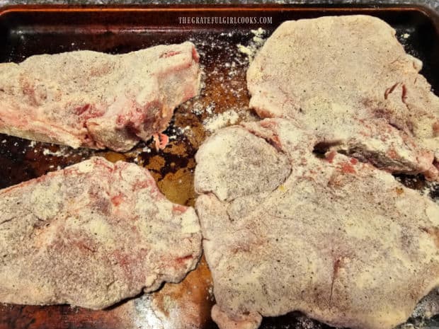 Four pork chops, coated with flour and spices, ready to be pan-seared.