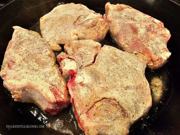 The seasoned pork chops cook in hot oil in a large skillet.