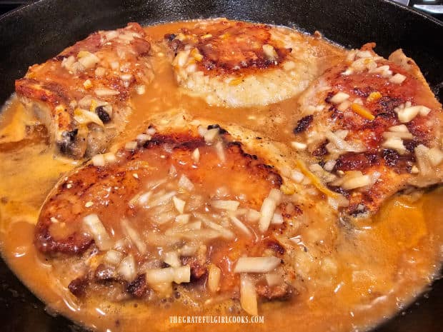 Sauce is poured over the browned pork chops in the skillet.