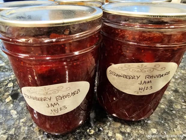 Jars of home canned strawberry rhubarb jam are labeled after cooling.