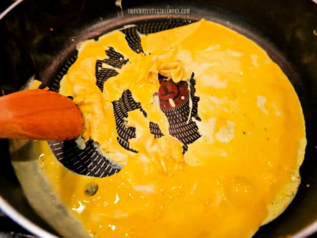 Three eggs are scrambled in hot oil in a large skillet.
