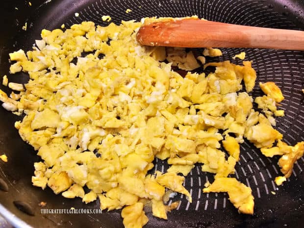 The scrambled eggs are chopped into very small pieces in skillet.
