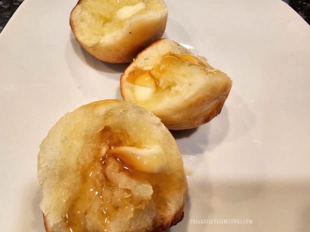 Pull apart cloverleaf dinner rolls with butter and honey, on a white plate.