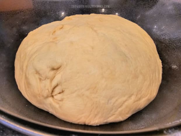 Bread dough placed in a large greased bowl to rise.