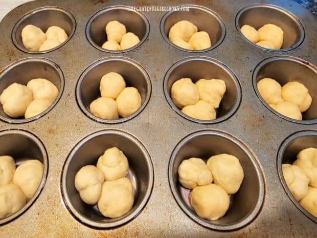Three balls of dough are put in each greased muffin cup.