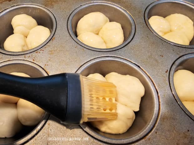 Melted butter is brushed on the cloverleaf dinner rolls before baking.