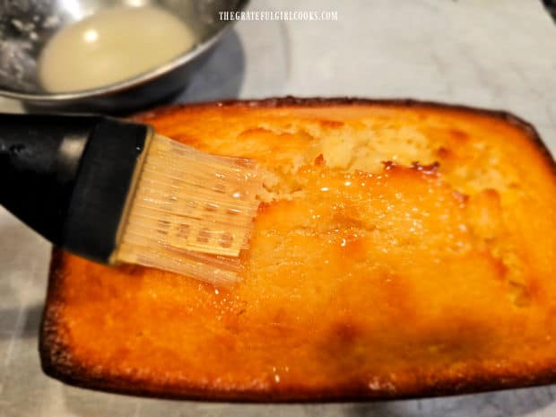 Lemon glaze is brushed over the top of the finished lemon coconut loaf.