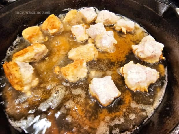 Battered chicken pieces are cooked and browned in hot oil in skillet.