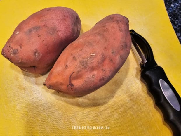 Two medium sweet potatoes on yellow mat, with a vegetable peeler.