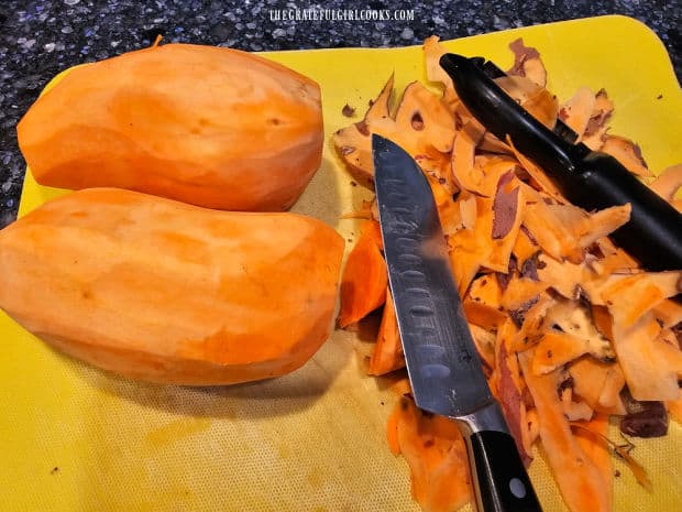 Two peeled sweet potatoes, with discarded peel, knife and vegetable peeler.