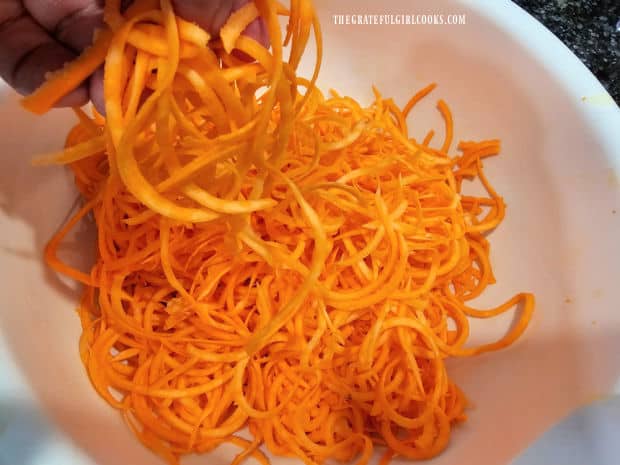 Spiralized sweet potato noodles fall into a large white bowl.