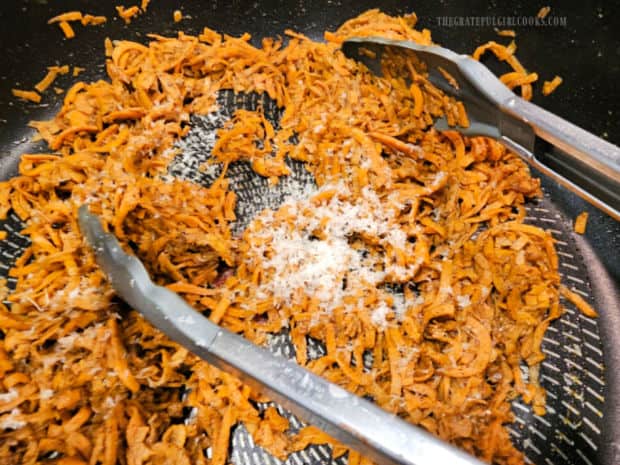 Grated Parmesan cheese is added to the sweet potato noodles in skillet.