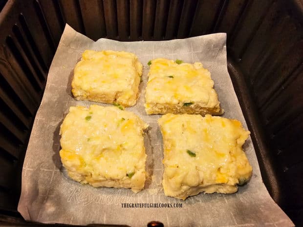 Biscuits on parchment paper in the air fryer basket in a preheated machine.