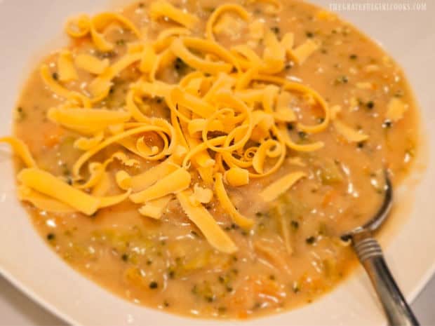 Grated cheddar cheese on top of a hot bowl of broccoli cheese soup.