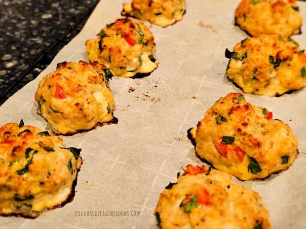 Eight chicken ricotta meatballs cool after baking on parchment paper.
